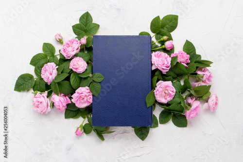 Book with a blue cover and pink roses on a light stone background. Flat lay, top view photo