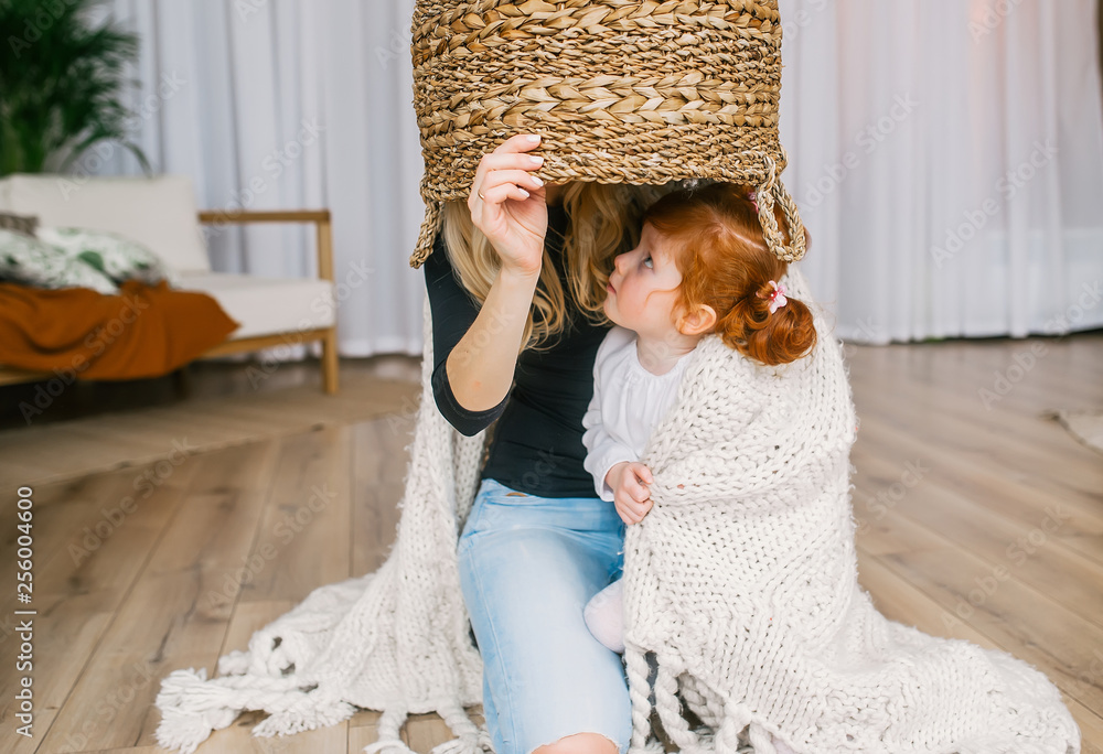 Mother and redhead girl playing home hide and seek, using big basket.
