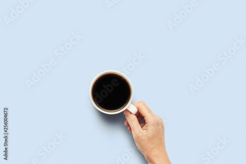Hand holding a cup with hot coffee on a blue background. Breakfast concept with coffee or tea. Good morning, night, insomnia. Flat lay, top view