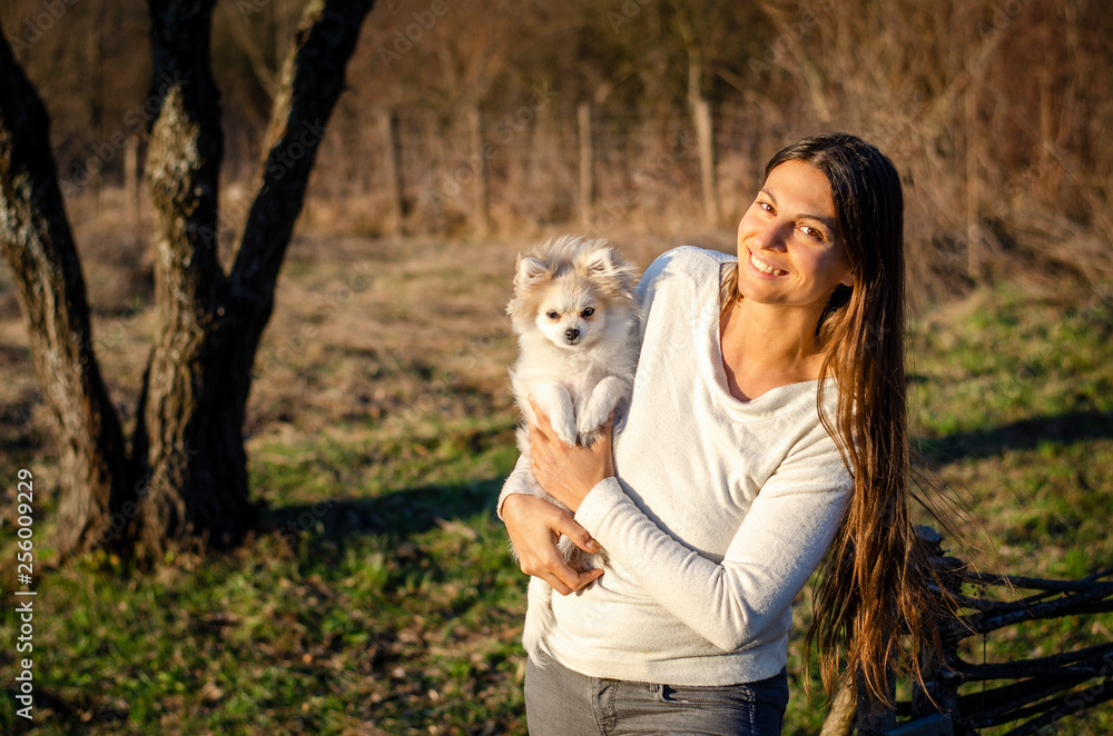 Beuatiful woman holding little pomenarian dog in the park.