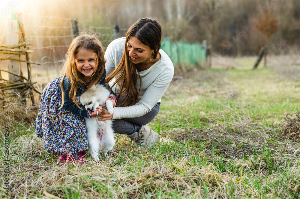 Mother and little girl laughing and playing with small dog outdoors Mother and little girl laughing and playing with small dog outdoors