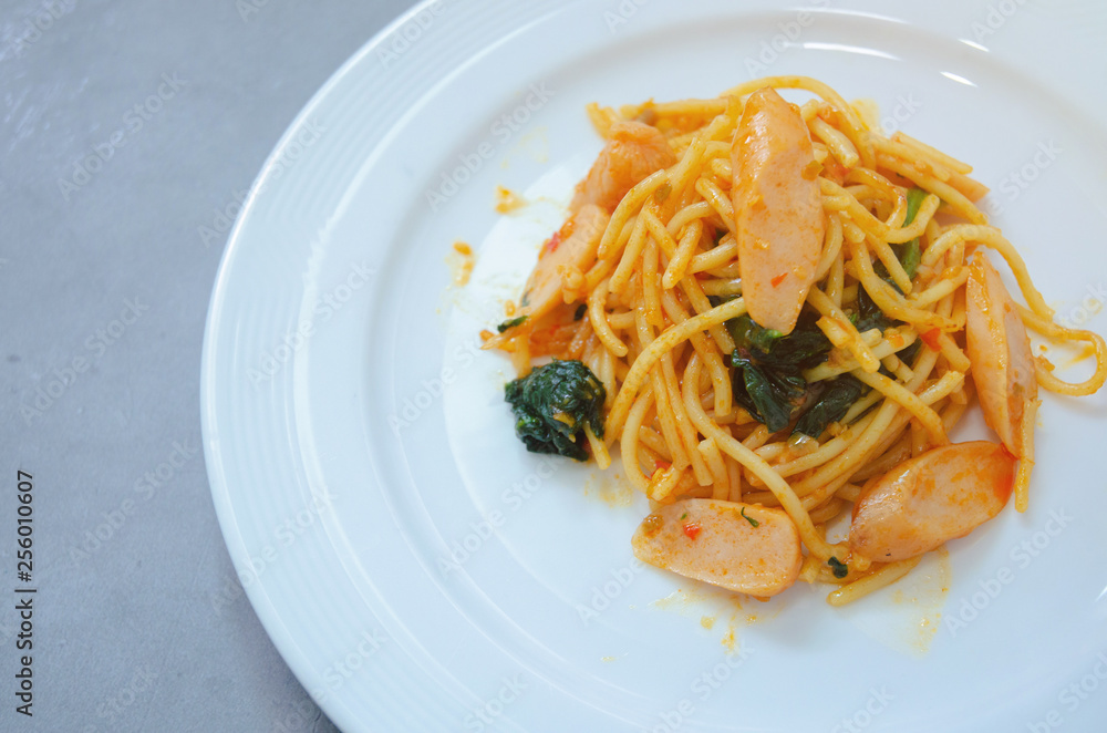 Spaghetti with sausage, Stir-fried sausage, Italian food.Spaghetti with red sauce, white plate on the table in the morning restaurant.