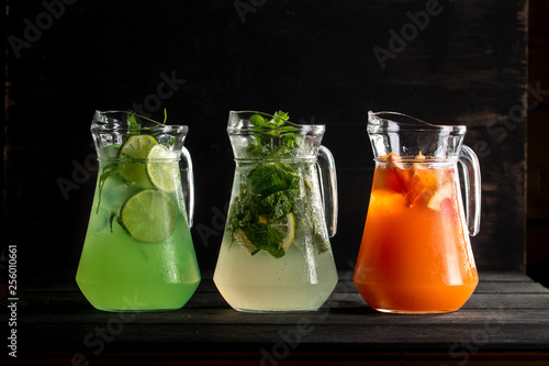 glass pitchers with different lemonade mojito, tarragon and orange on black background