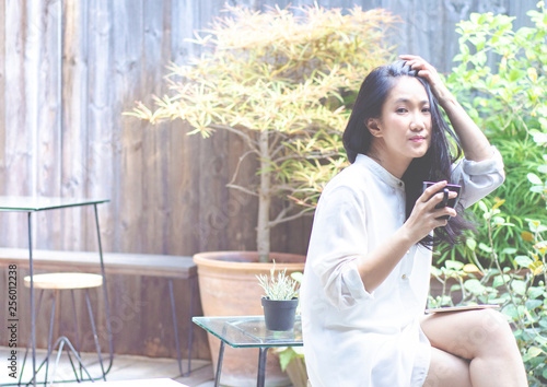 Asian women wear white shirts. She is drinking coffee in the morning garden.Black coffee mug in hand.In the garden there is a girl sitting.Do not focus on objects..