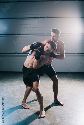 strong muscular mma fighter doing chokehold to sportive shirtless opponent