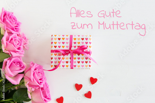 Muttertagskarte mit Rosen und Herzen auf weissem Holzhintergrund, Geschenkbox mit Schleife