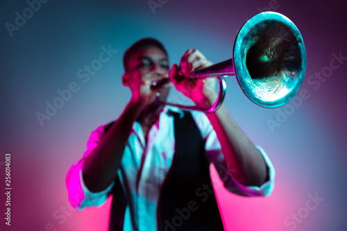 African American handsome jazz musician playing trumpet in the studio on a neon background. Music concept. Young joyful attractive guy improvising. Close-up retro portrait.