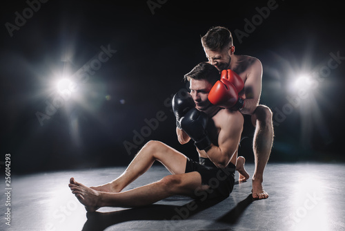 Tableau sur toile strong mma fighter in boxing gloves doing painful chokehold to another sportsman