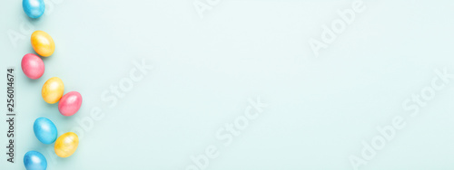 Border made of colorful Easter eggs on turquoise background. Top view, copy spase, minimal styled banner for website.