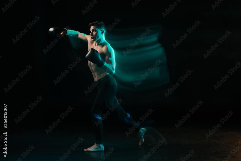 Fototapeta premium Long exposure of green light and sporty muscular mma fighter doing punch on black