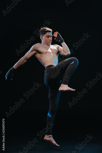 muscular shirtless strenuous mma fighter in bandages jumping isolated on black