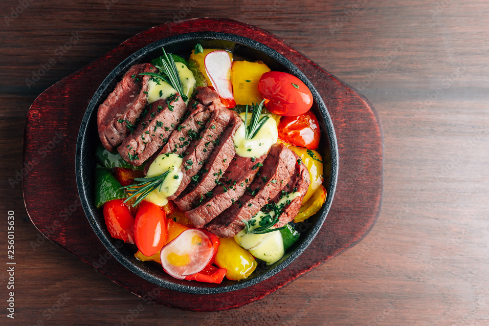Φωτογραφία Top view of medium rare beef steak served in hot plate with tomato, bell pepper, radish and rosemary