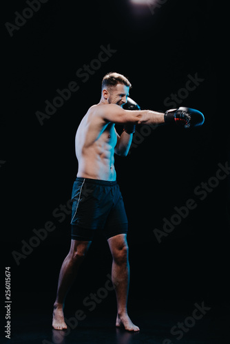 barefoot sporty boxer with strenuous face expression in boxing gloves doing punch isolated on black © LIGHTFIELD STUDIOS