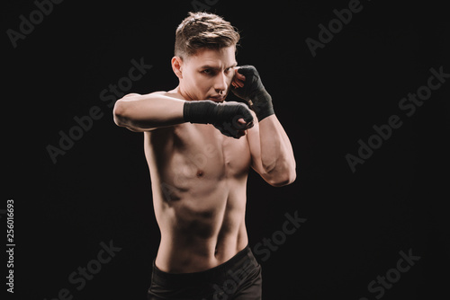 strong confident mma fighter in bandages doing punch isolated on black