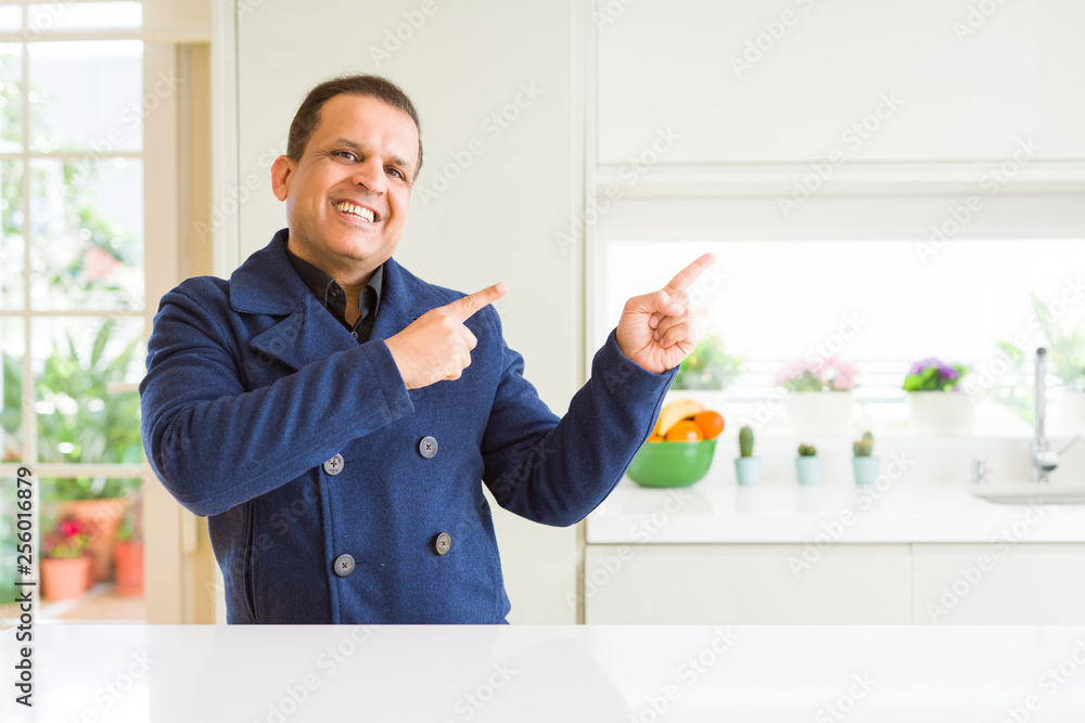Middle age man sitting at home smiling and looking at the camera pointing with two hands and fingers to the side. Middle age man sitting at home smiling and looking at the camera pointing with two hands and fingers to the side.