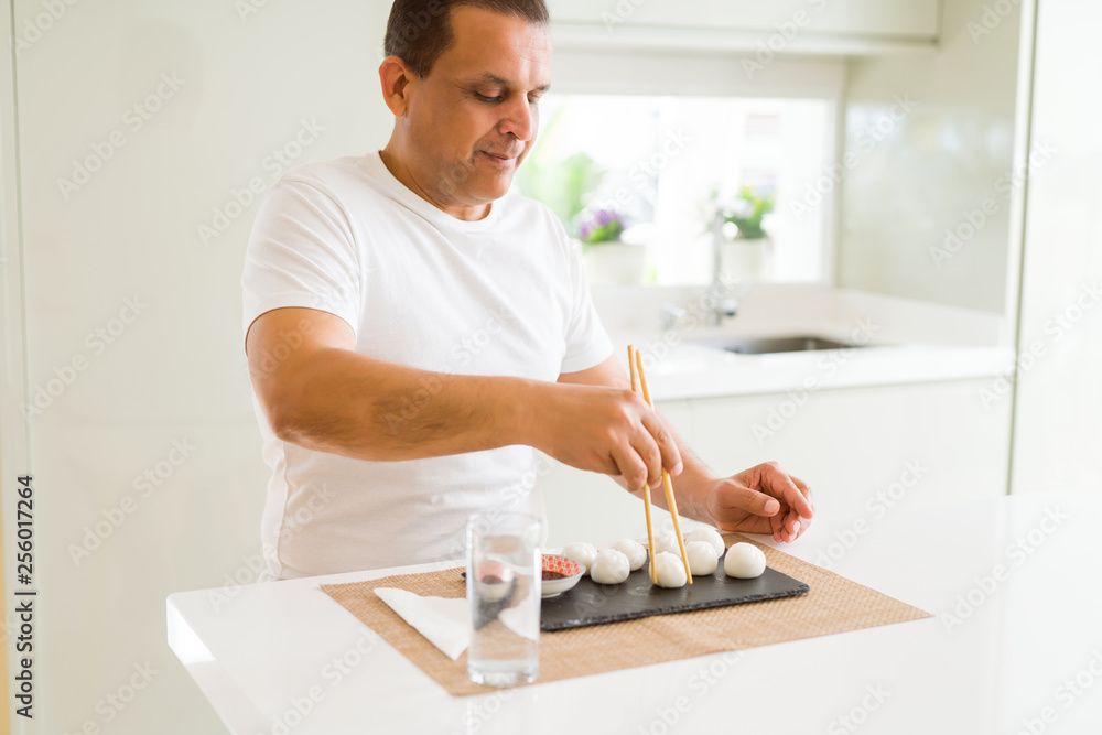 Middle age man eating asian dim sum using chopsticks at home Middle age man eating asian dim sum using chopsticks at home