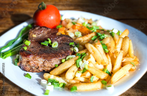 Steak, fried potatoes, greens and tomato on a plate close up