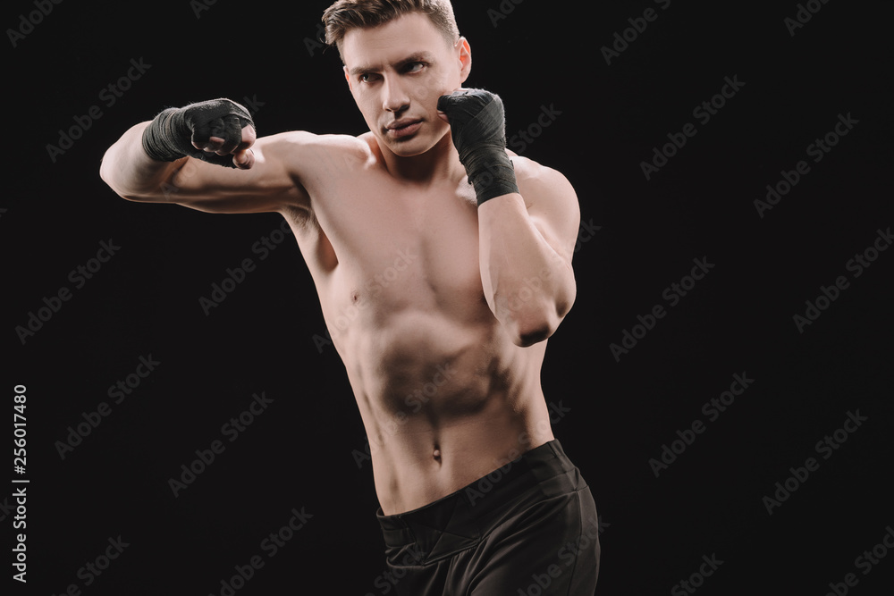 strong athletic muscular sportsman in bandages doing punch isolated on black