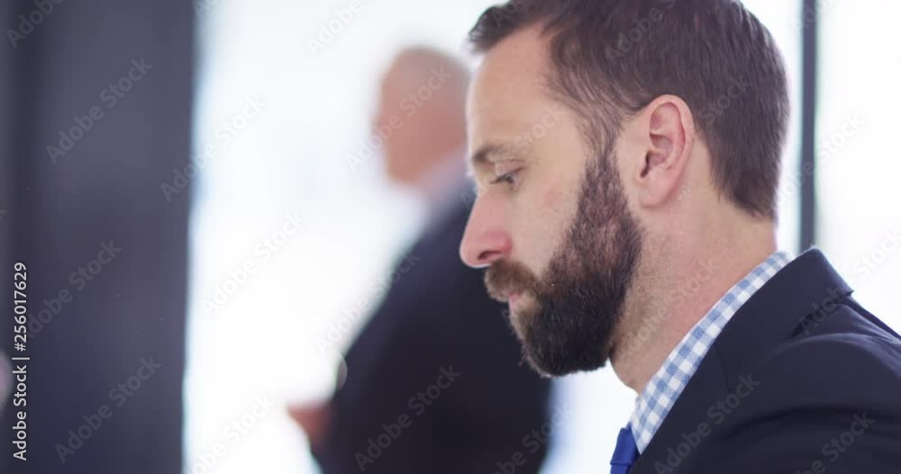 4K Closeup businessman working at his desk with colleagues talking in background 4K Closeup businessman working at his desk with colleagues talking in background