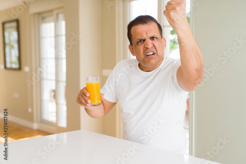 Obraz na plátně Middle age man drinking a glass of orange juice at home annoyed and frustrated s