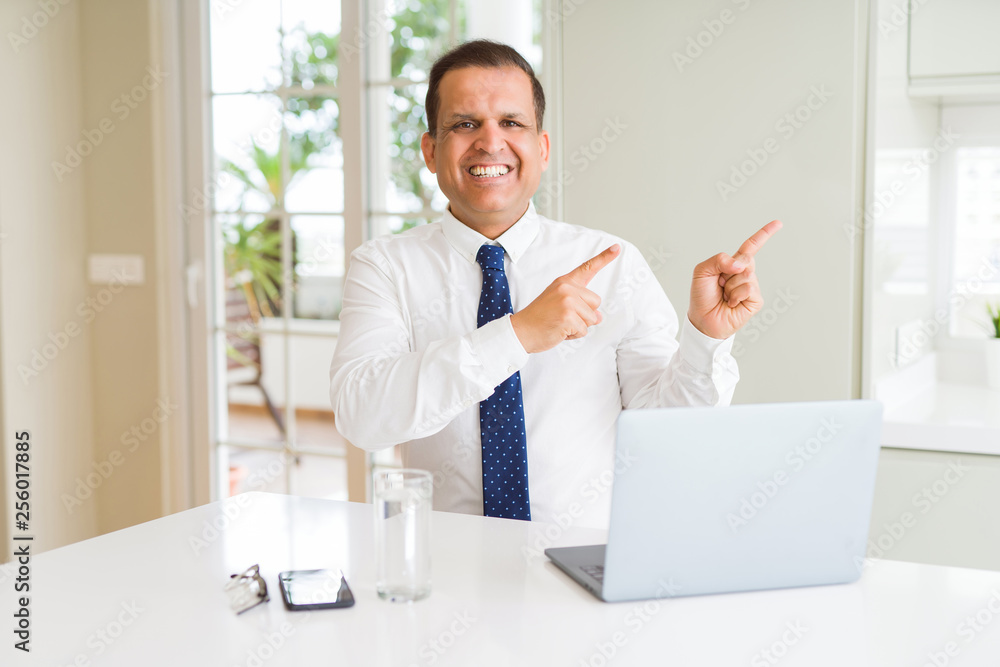 Middle age business man working with computer laptop smiling and looking at the camera pointing with two hands and fingers to the side.