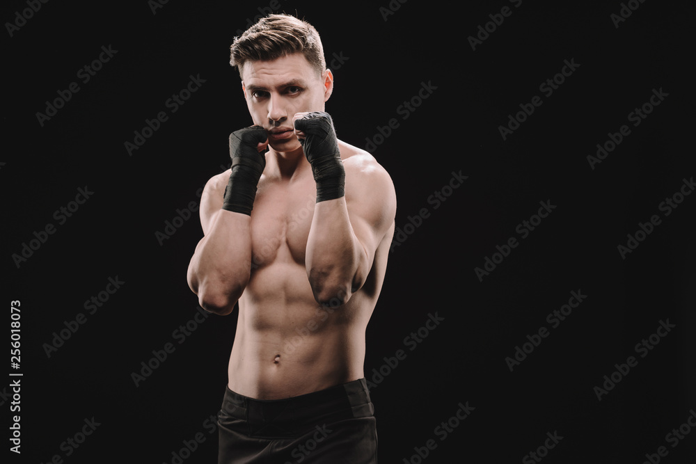 strong shirtless muscular sportsman in bandages doing block isolated on black