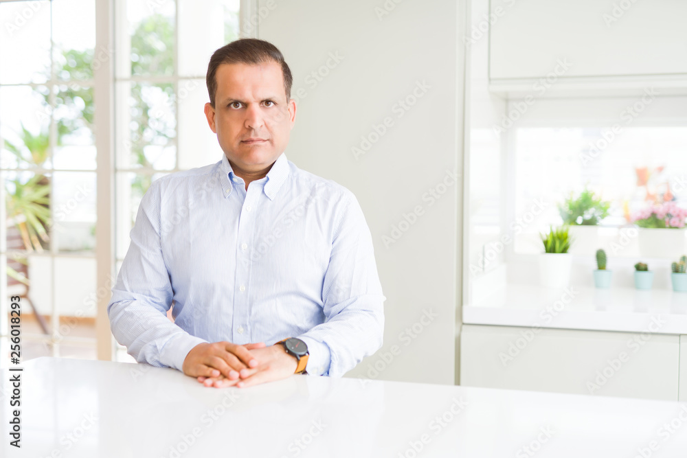 Middle age man sitting at home Relaxed with serious expression on face. Simple and natural looking at the camera.