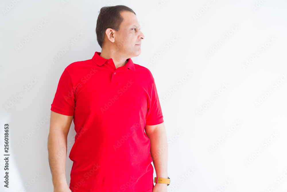 Middle age man wearing red t-shirt over white wall looking to side, relax profile pose with natural face with confident smile. Middle age man wearing red t-shirt over white wall looking to side, relax profile pose with natural face with confident smile.
