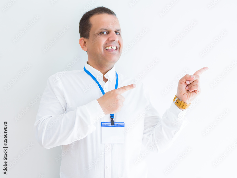Middle age business man wearing ID card over white background smiling and looking at the camera pointing with two hands and fingers to the side. Middle age business man wearing ID card over white background smiling and looking at the camera pointing with two hands and fingers to the side.