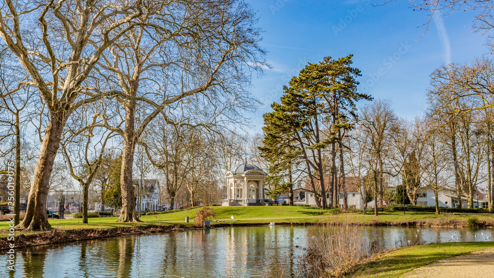 View of a pond, green grass with tea cupola or Gloriette on a hill in the background in the park Proosdij, sunny winter day in Meerssen south Limburg in the Netherlands