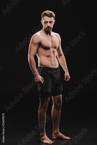 strong athletic barefoot muscular sportsman looking at camera on black