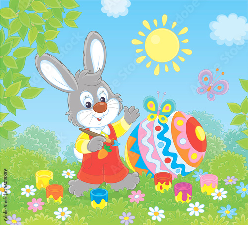 Little grey bunny coloring a big Easter egg on green grass among flowers on a sunny spring day, vector illustration in a cartoon style