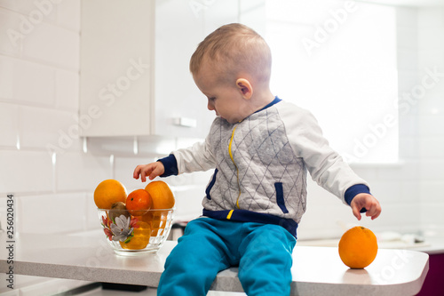 Cute toddler with fruits in kitchen.