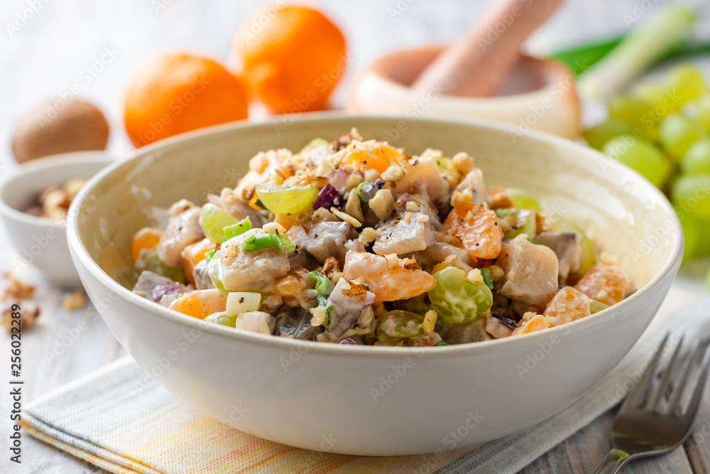 Salad with herring, tangerines, grapes, onions and walnuts in bowl on wooden table. Selective focus.