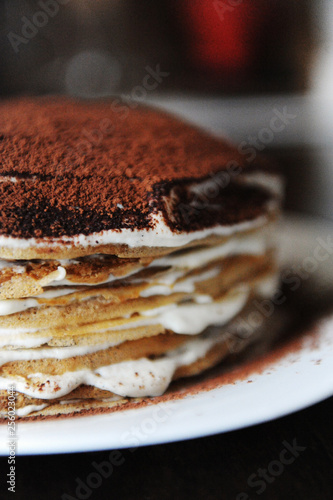 Crepe cake with tiramisu filling dusted with powdery cocoa. White plate, background of coffee house. Half cake close up