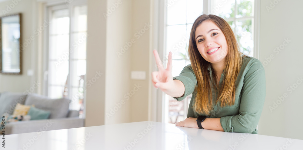 Beautiful young woman at home smiling looking to the camera showing fingers doing victory sign. Number two. Beautiful young woman at home smiling looking to the camera showing fingers doing victory sign. Number two.