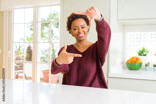 Young beautiful african american woman at home smiling making frame with hands and fingers with happy face. Creativity and photography concept.
