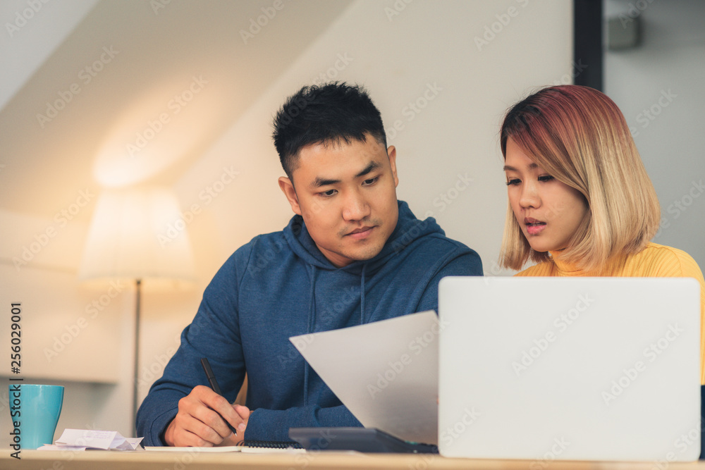Young asian couple managing finances, reviewing their bank accounts using laptop computer and calculator at modern home. Woman and man doing paperwork together, paying taxes online on notebook pc. Young asian couple managing finances, reviewing their bank accounts using laptop computer and calculator at modern home. Woman and man doing paperwork together, paying taxes online on notebook pc.