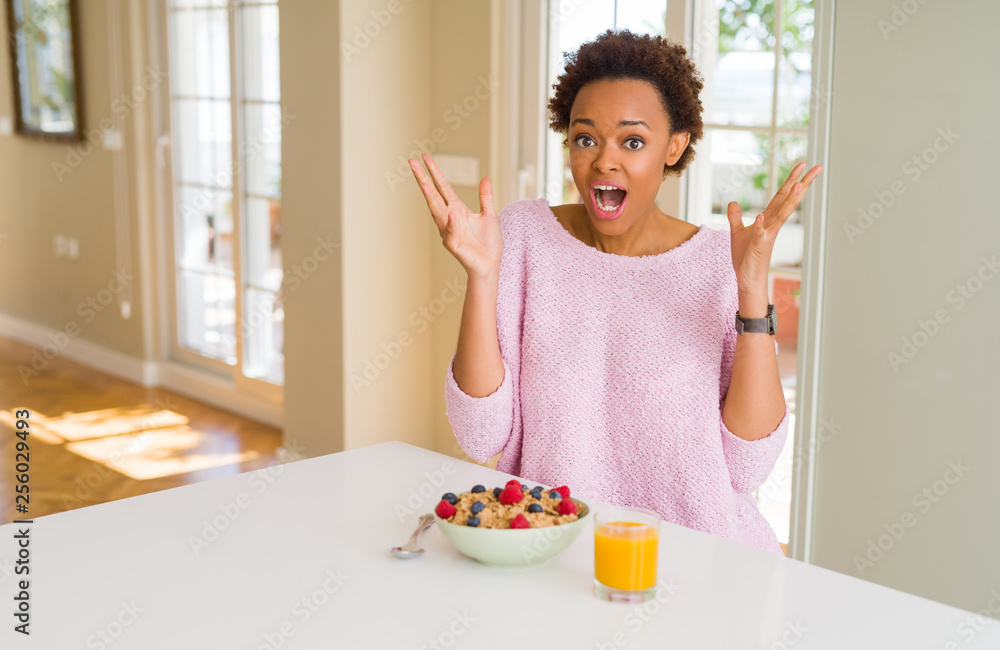 Young african american woman having healthy breakfast in the morning at home celebrating crazy and amazed for success with arms raised and open eyes screaming excited. Winner concept Young african american woman having healthy breakfast in the morning at home celebrating crazy and amazed for success with arms raised and open eyes screaming excited. Winner concept