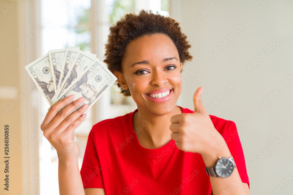 Young african american woman holding bank notes of twenty dollars happy with big smile doing ok sign, thumb up with fingers, excellent sign Young african american woman holding bank notes of twenty dollars happy with big smile doing ok sign, thumb up with fingers, excellent sign