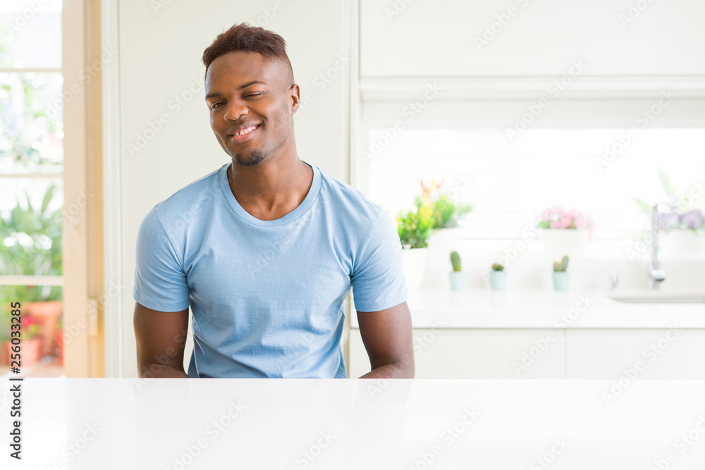 Handsome african american man wearing casual t-shirt at home winking looking at the camera with sexy expression, cheerful and happy face. Handsome african american man wearing casual t-shirt at home winking looking at the camera with sexy expression, cheerful and happy face.