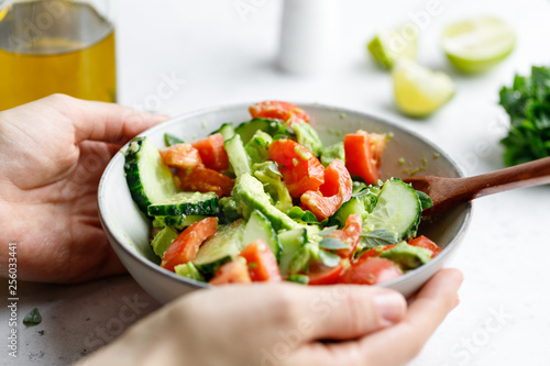 Hands hold vegetarian salad is made from avocado, tomatoes, cucumber, basil and lime juice.