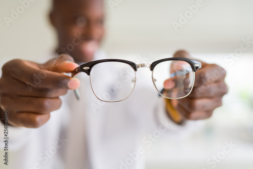 African american optiian man holding and showing glasses lens to custumers at the optics shop while smiling confident
