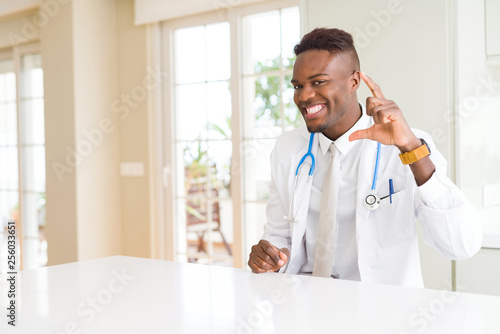 African american doctor man at the clinic smiling and confident gesturing with hand doing size sign with fingers while looking and the camera. Measure concept.