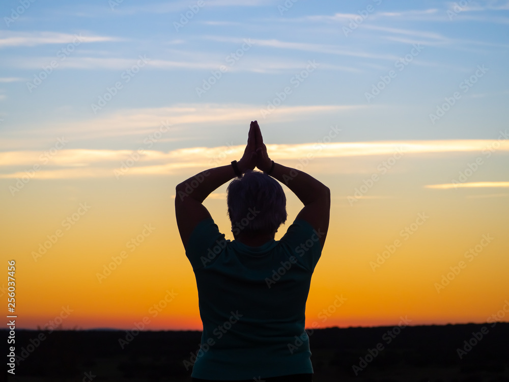 A senior woman practicing yoga at sunset