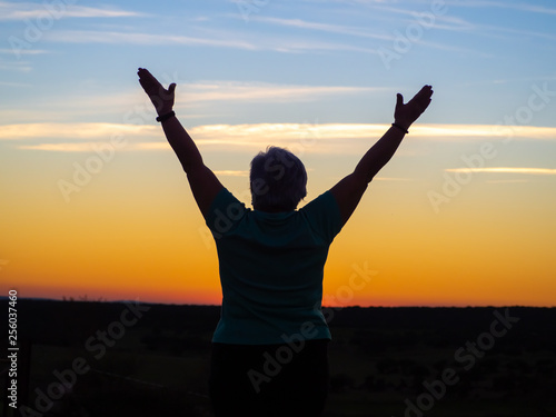 A senior woman practicing yoga at sunset