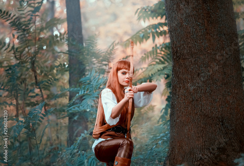 new image of Robin Hood as girl hunter, attractive lady in white shirt and leather pants pulled bow before shot at target, confident earner with red hair prepared arrow, bright photo in green forest