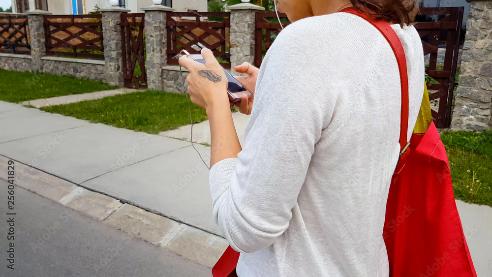 Obraz premium Female student earphones looking in smartphone app, walking street, life danger