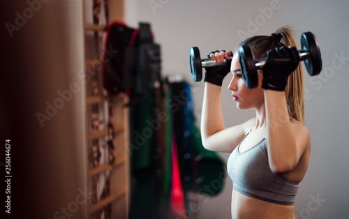 Young girl or woman with dumbbells, doing workout in a gym. © Halfpoint