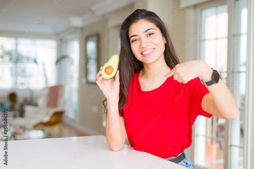 Young woman eating healthy avocado with surprise face pointing finger to himself Young woman eating healthy avocado with surprise face pointing finger to himself